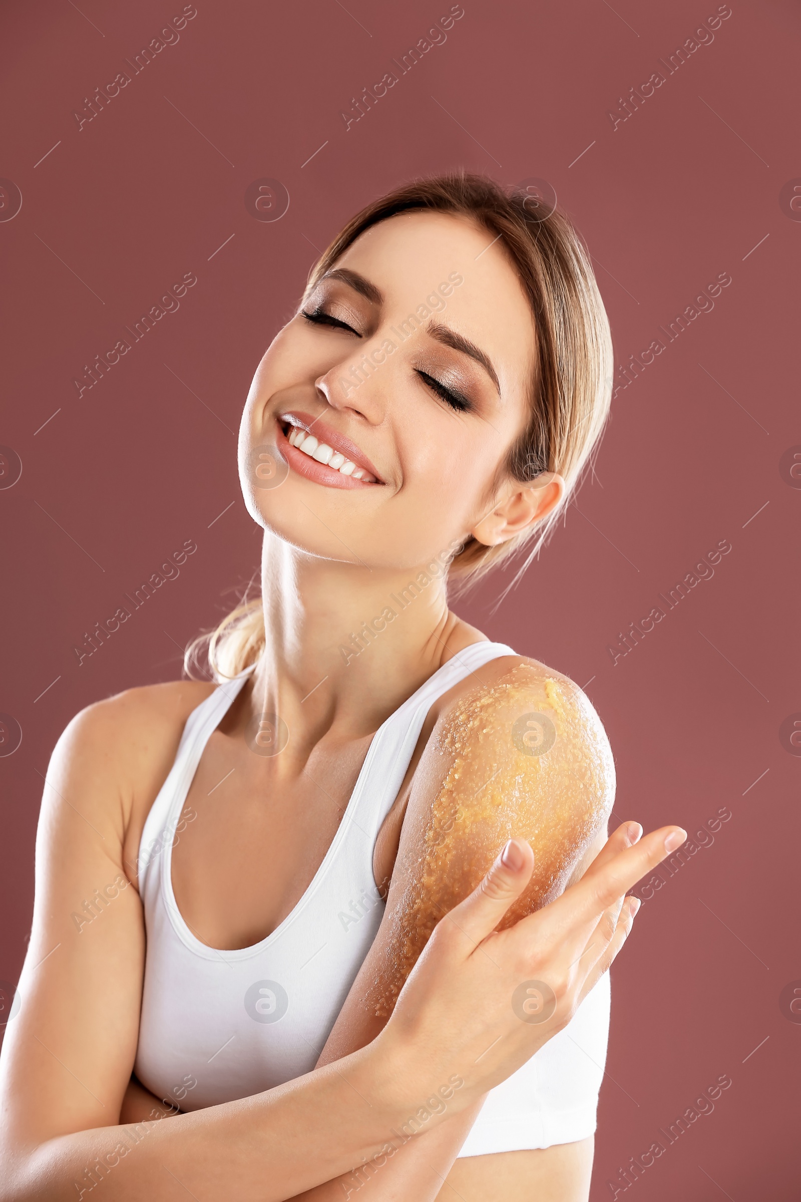 Photo of Young woman applying natural scrub on her shoulder against color background