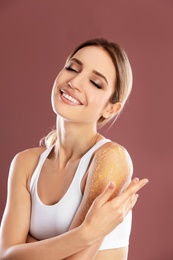 Young woman applying natural scrub on her shoulder against color background