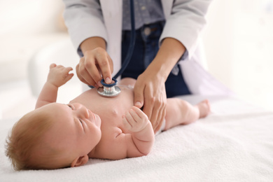 Photo of Doctor examining cute baby with stethoscope indoors, closeup. Health care