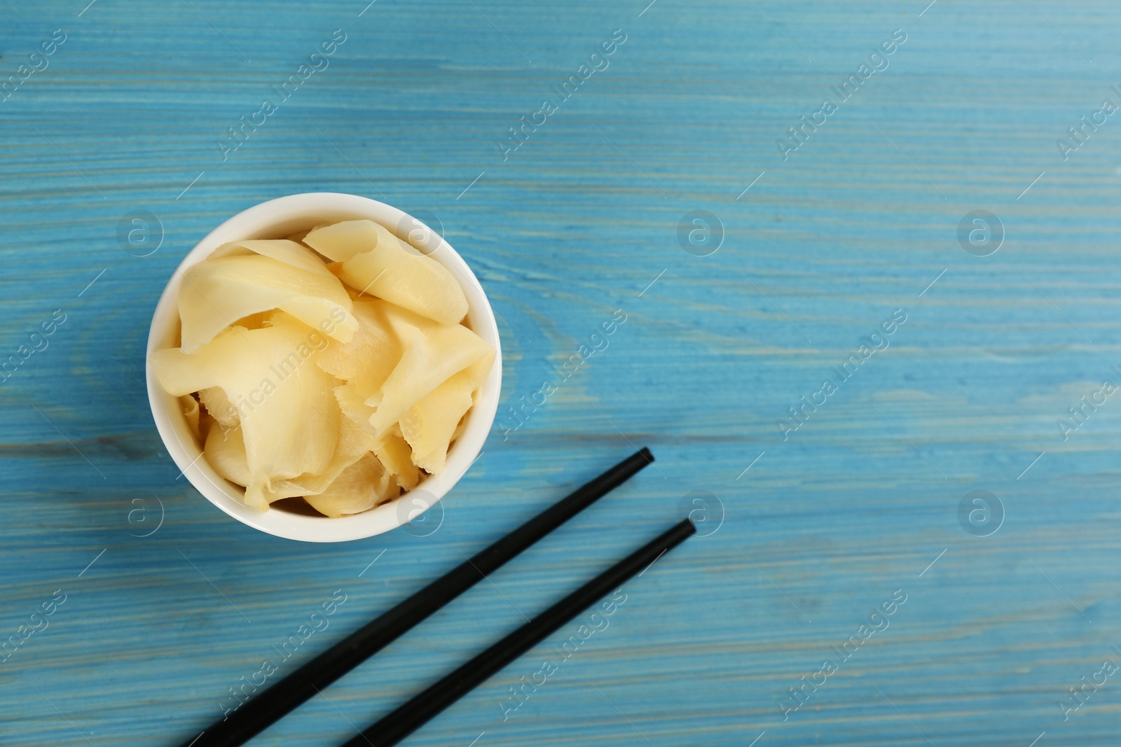 Photo of Spicy pickled ginger and chopsticks on light blue wooden table, flat lay. Space for text