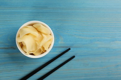 Spicy pickled ginger and chopsticks on light blue wooden table, flat lay. Space for text