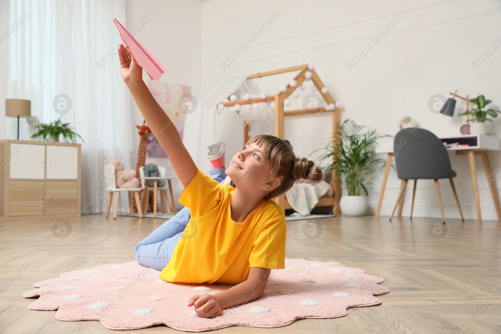 Photo of Cute little girl playing with paper plane on floor in room