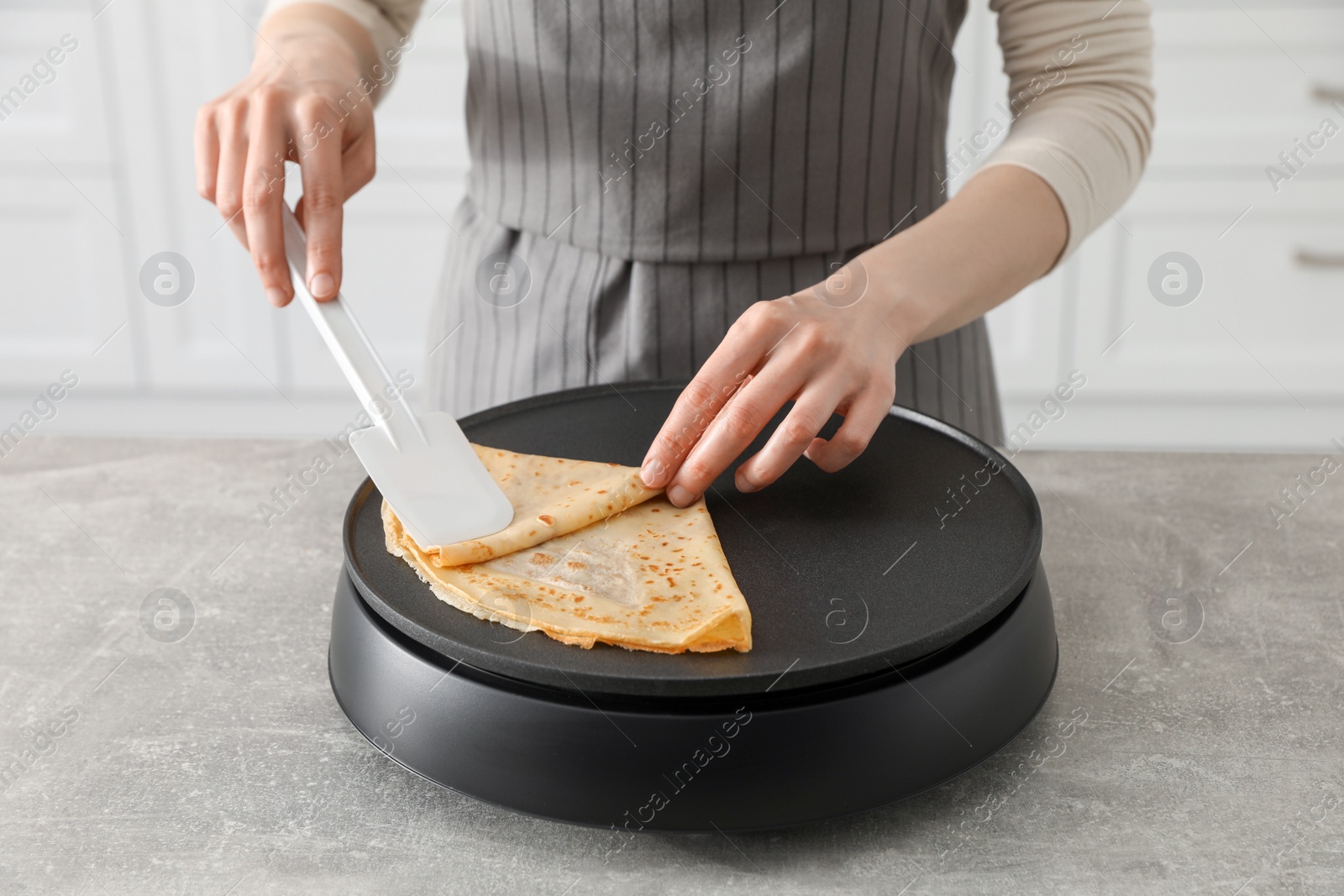 Photo of Woman cooking delicious crepe on electric pancake maker in kitchen, closeup