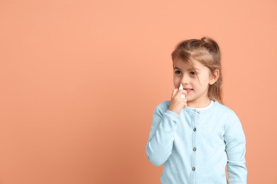 Photo of Sick little girl using nasal spray on coral background. Space for text