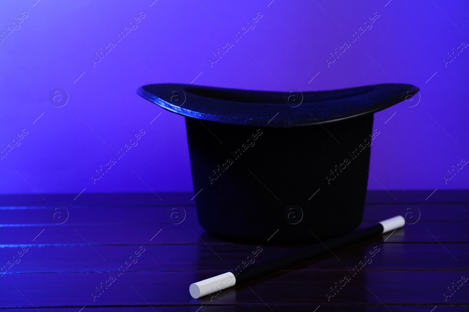 Photo of Black top hat and wand on wooden table, space for text. Magician equipment