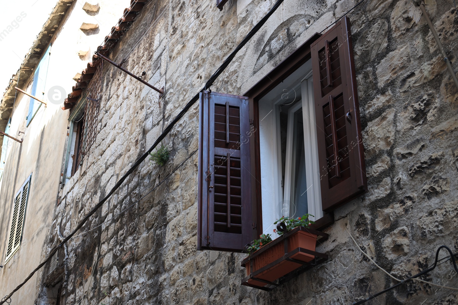 Photo of Old residential building with open window and flowers growing in holder, low angle view