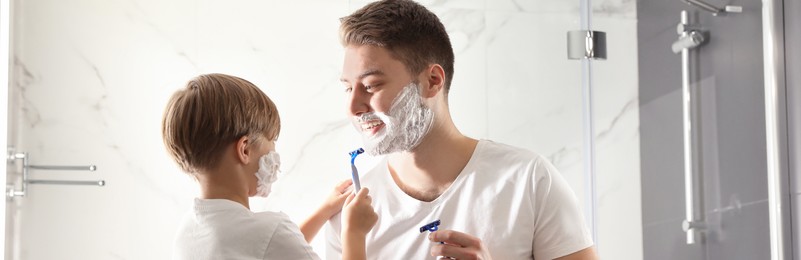 Image of Dad and son with shaving foam on their faces having fun in bathroom. Banner design