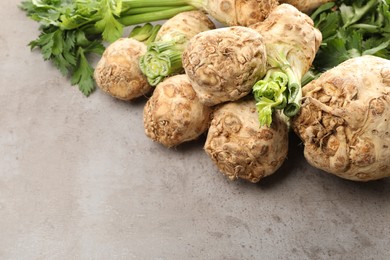 Many raw celery roots and leaves on grey table, space for text