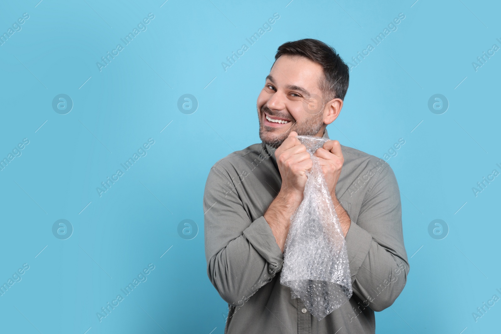 Photo of Happy man with bubble wrap on light blue background. Space for text