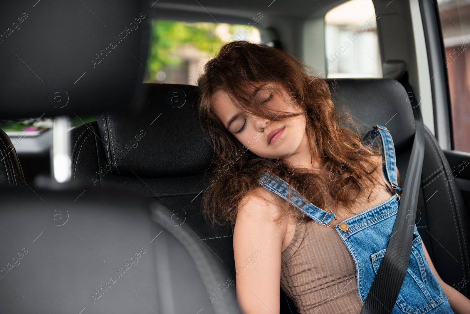 Photo of Tired girl with fastened seat belt sleeping in car