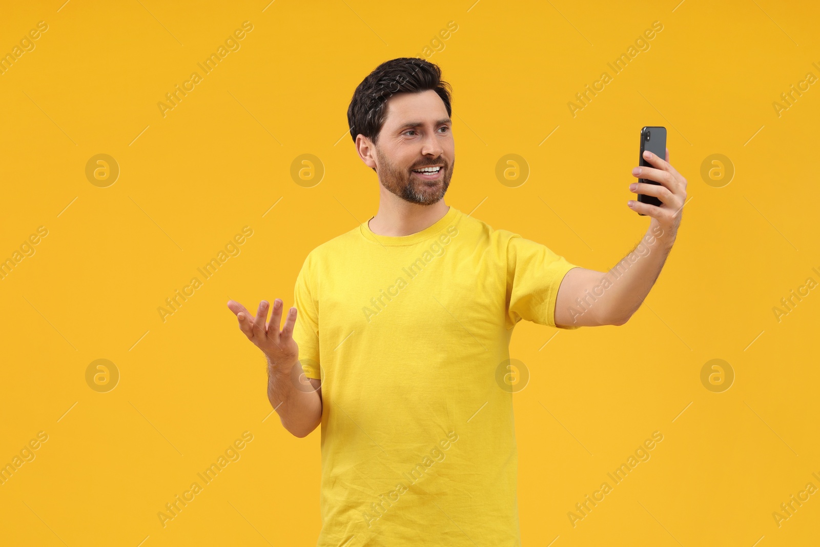 Photo of Smiling man taking selfie with smartphone on yellow background