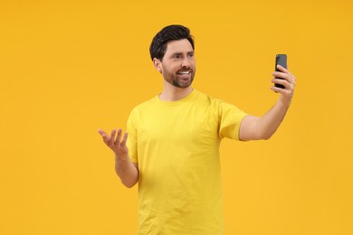 Smiling man taking selfie with smartphone on yellow background