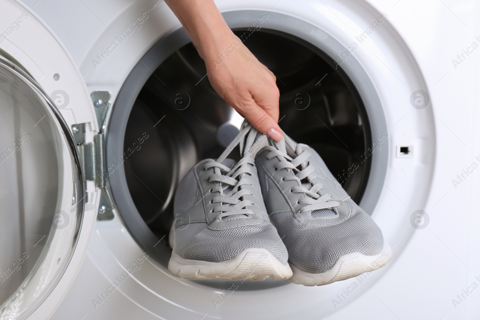 Photo of Woman putting pair of sport shoes into washing machine, closeup