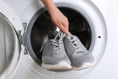 Woman putting pair of sport shoes into washing machine, closeup