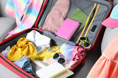 Photo of Open suitcase with stylish clothes and accessories on grey sofa. Summer vacation