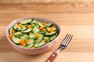 Photo of Tasty fresh salad with cucumber in bowl and fork on wooden table