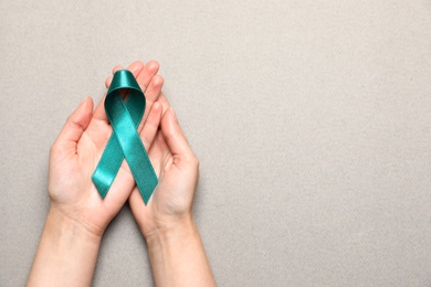 Woman holding teal awareness ribbon on grey paper, top view with space for text. Symbol of social and medical issues