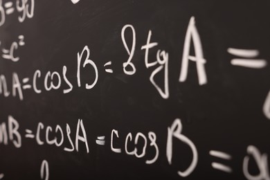 Different mathematical formulas written with chalk on blackboard, closeup