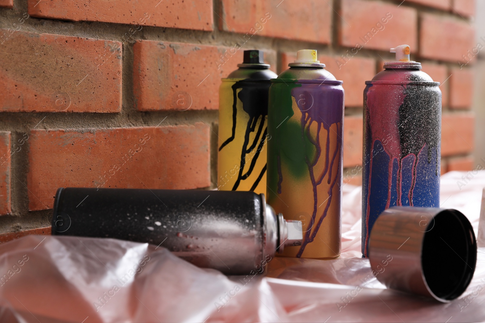 Photo of Used cans of spray paints on table near brick wall. Graffiti supplies