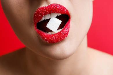 Photo of Woman with beautiful lips eating sugar cube on red background, closeup