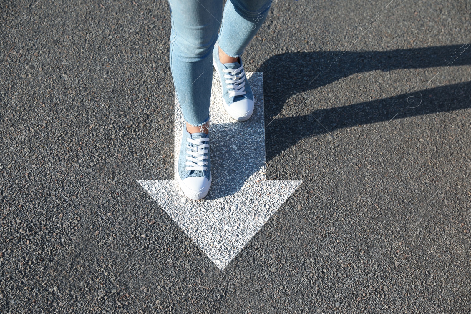 Image of Planning future. Woman walking on drawn mark on road, closeup. White arrow showing direction of way