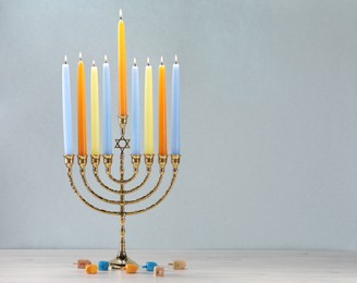 Photo of Hanukkah celebration. Menorah with burning candles and dreidels on wooden table against white background, closeup. Space for text
