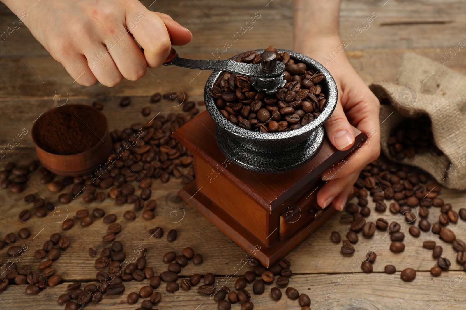 Photo of Woman using manual coffee grinder at wooden table, closeup