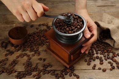 Photo of Woman using manual coffee grinder at wooden table, closeup