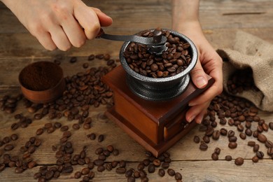 Woman using manual coffee grinder at wooden table, closeup