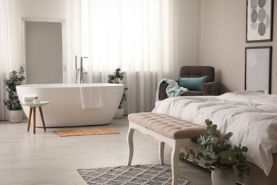 Stylish light apartment interior with white bathtub and bed