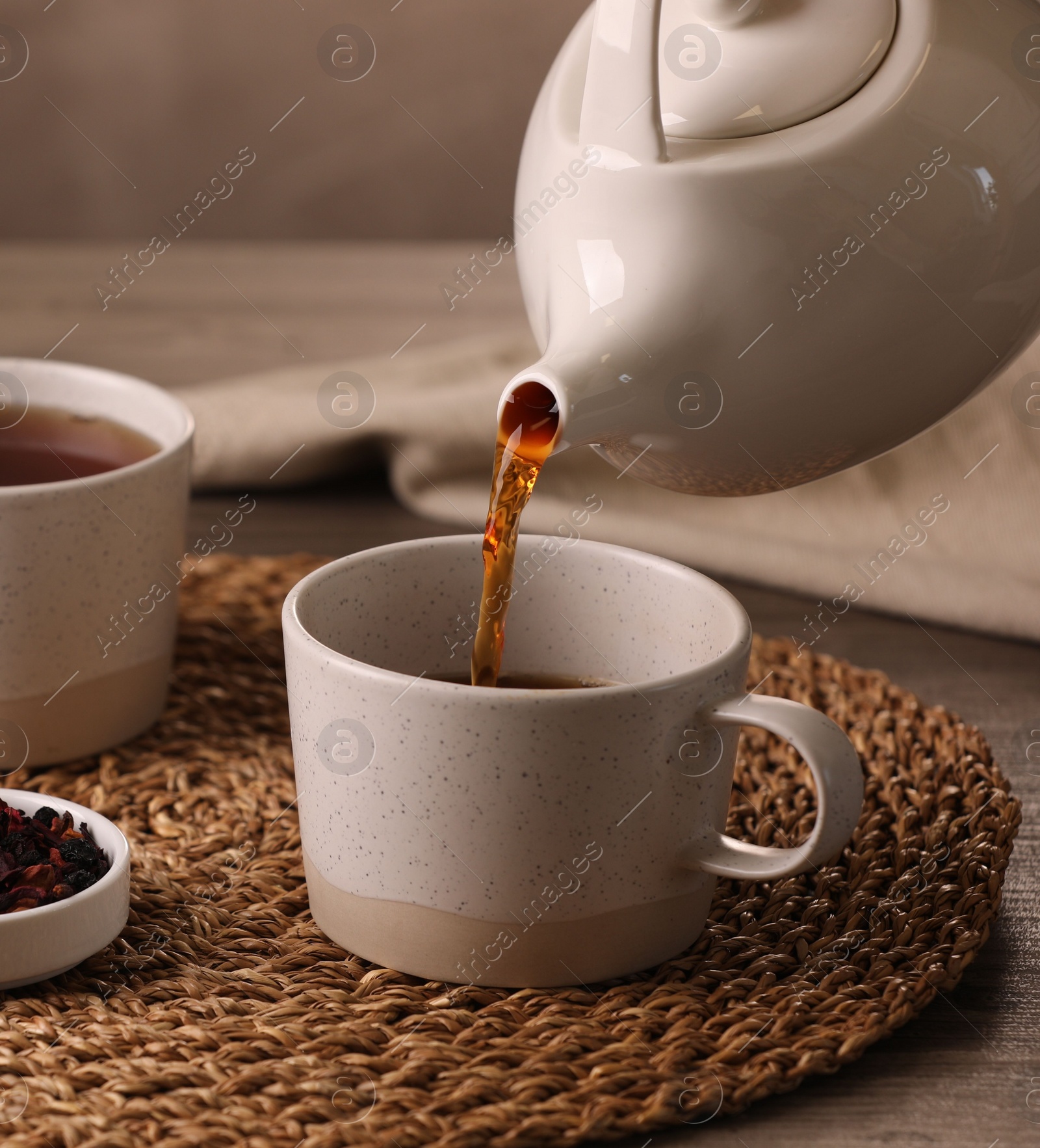 Photo of Pouring aromatic tea into cup at table, closeup