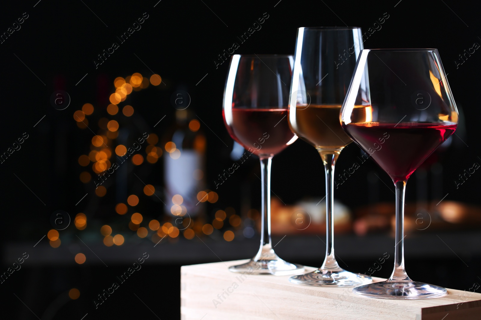 Photo of Glasses with different wines on wooden table against defocused lights. Space for text