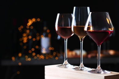 Glasses with different wines on wooden table against defocused lights. Space for text