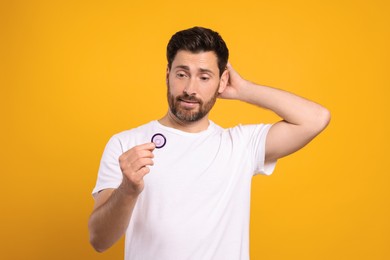 Photo of Confused man holding condom on yellow background. Safe sex