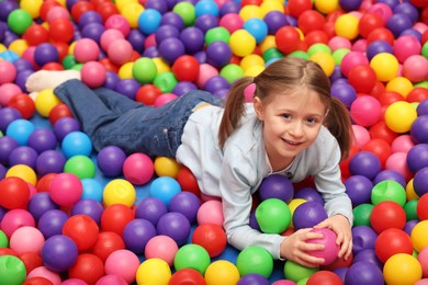 Photo of Happy little girl lying on many colorful balls in ball pit