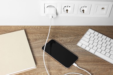 Photo of Modern smartphone charging on wooden table, above view