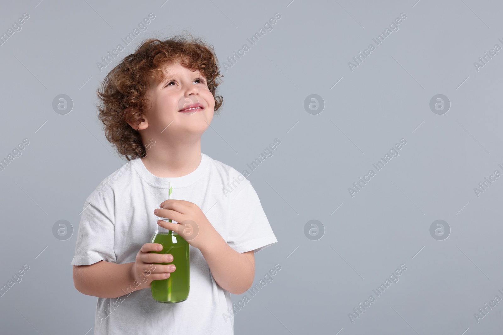 Photo of Cute little boy with glass bottle of fresh juice on light gray background, space for text