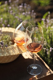 Photo of Straw hat and glasses of wine on wooden table in lavender field