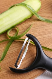 Photo of Fresh cucumber, peels and peeler on white table, closeup