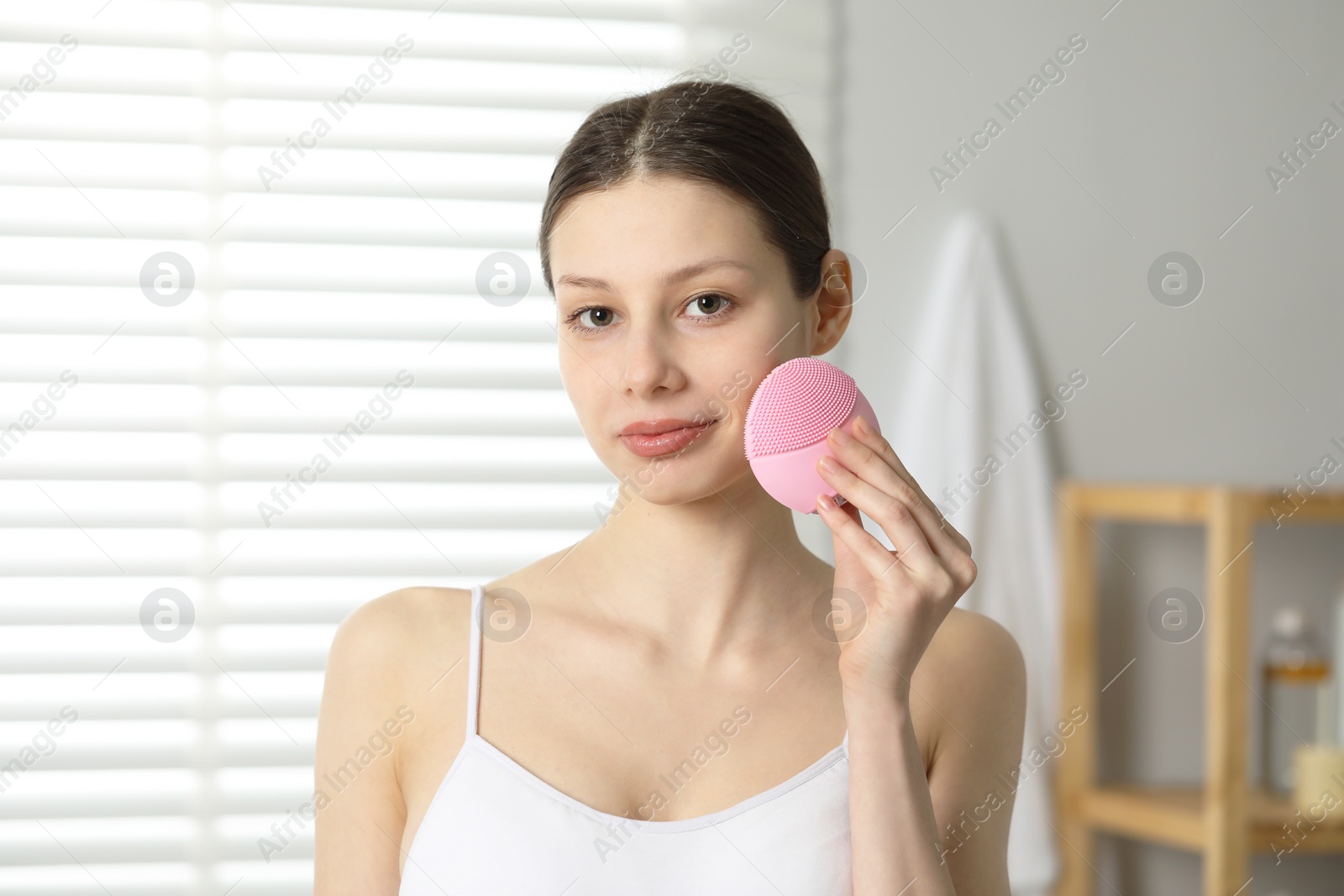 Photo of Washing face. Young woman with cleansing brush indoors