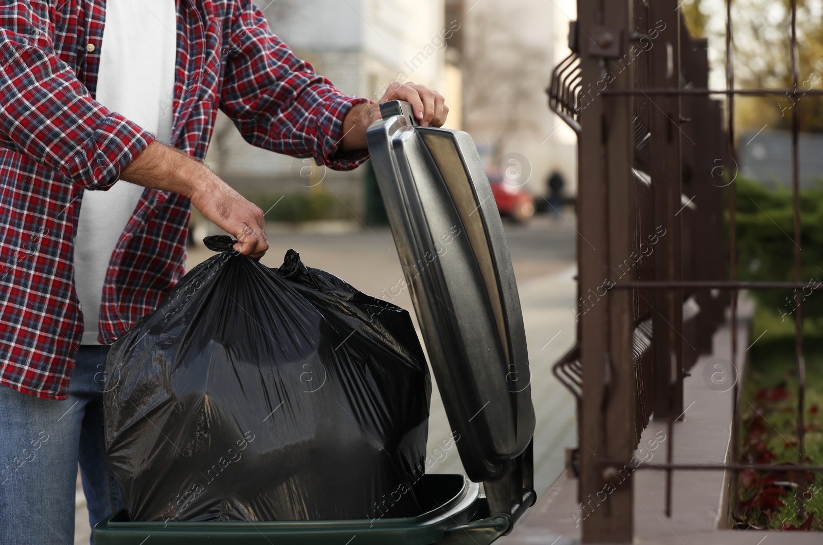 Photo of Man putting garbage bag into recycling bin outdoors, closeup