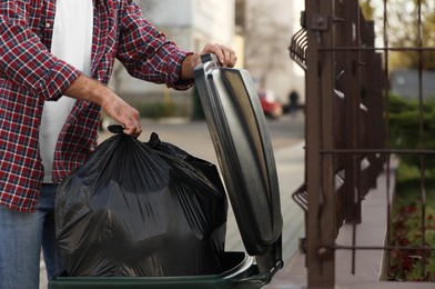 Photo of Man putting garbage bag into recycling bin outdoors, closeup