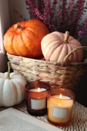 Photo of Beautiful heather flowers, burning candles, open book and wicker basket with pumpkins indoors