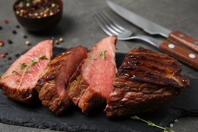 Board with slices of grilled meat on grey table, closeup