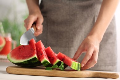 Photo of Woman cutting delicious watermelon at white wooden table indoors, closeup