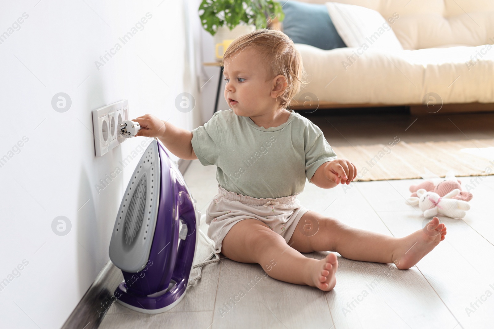 Photo of Cute baby playing with electrical socket and iron plug at home. Dangerous situation