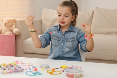 Photo of Cute little girl making beaded jewelry at table in room