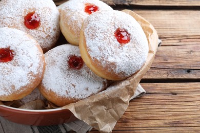 Delicious donuts with jelly and powdered sugar in baking dish on wooden table, closeup
