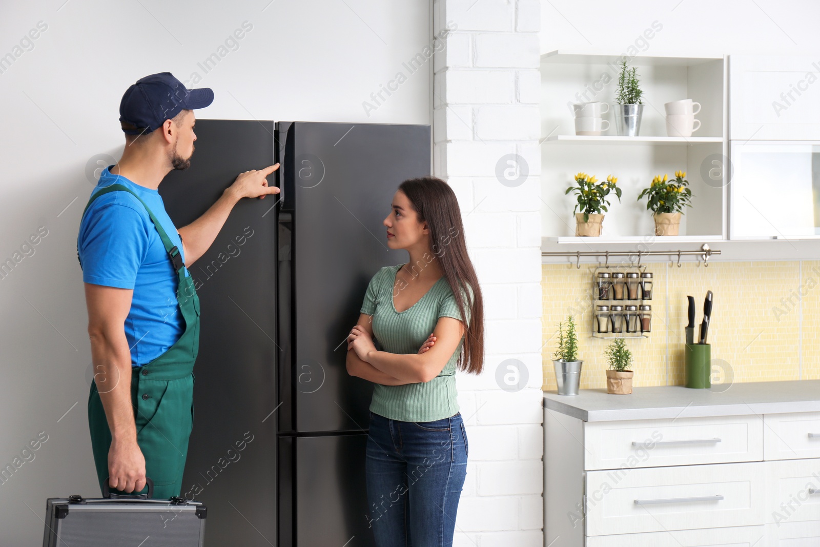 Photo of Male technician talking with client near refrigerator in kitchen