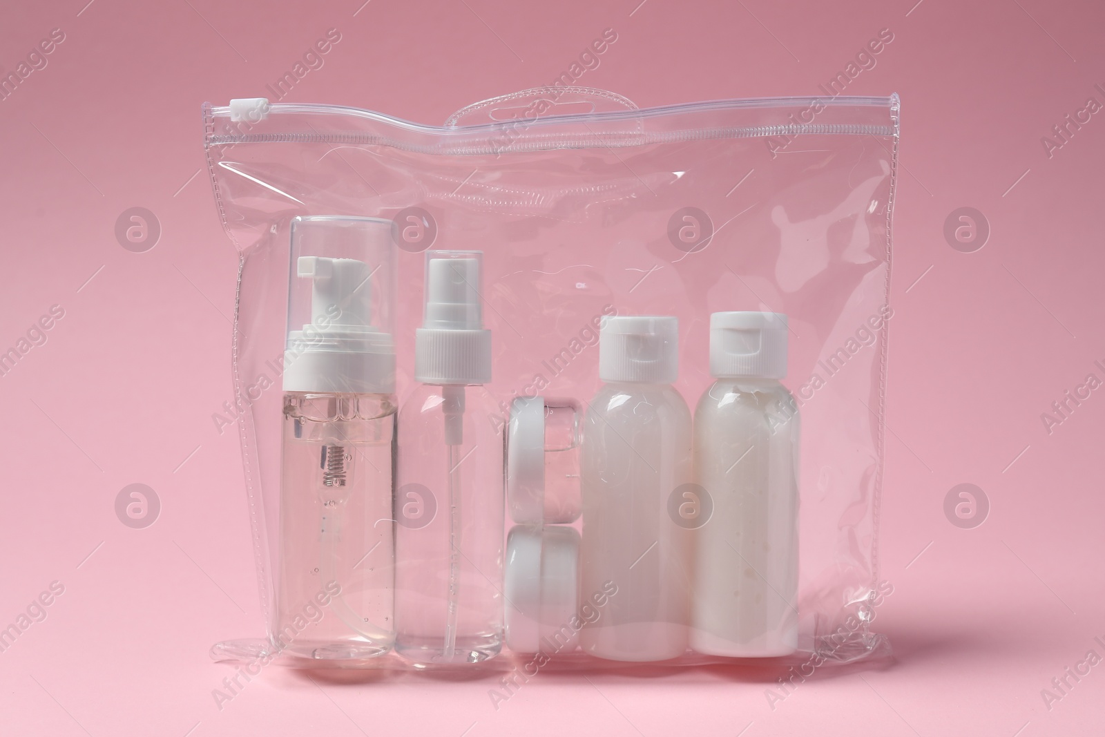 Photo of Cosmetic travel kit in plastic bag on pink background. Bath accessories